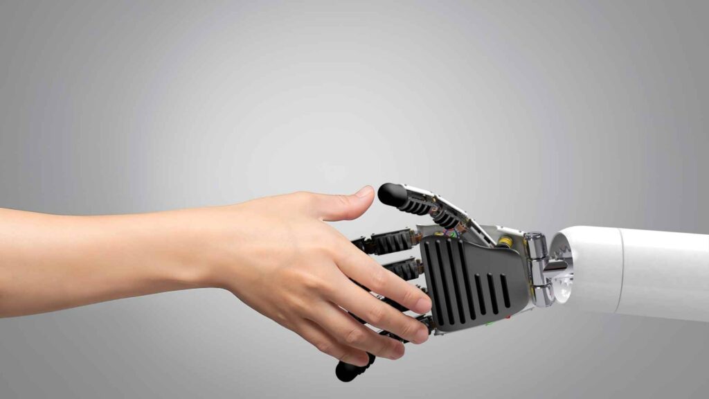 A human hand and a robotic hand reaching out to shake hands against a neutral background