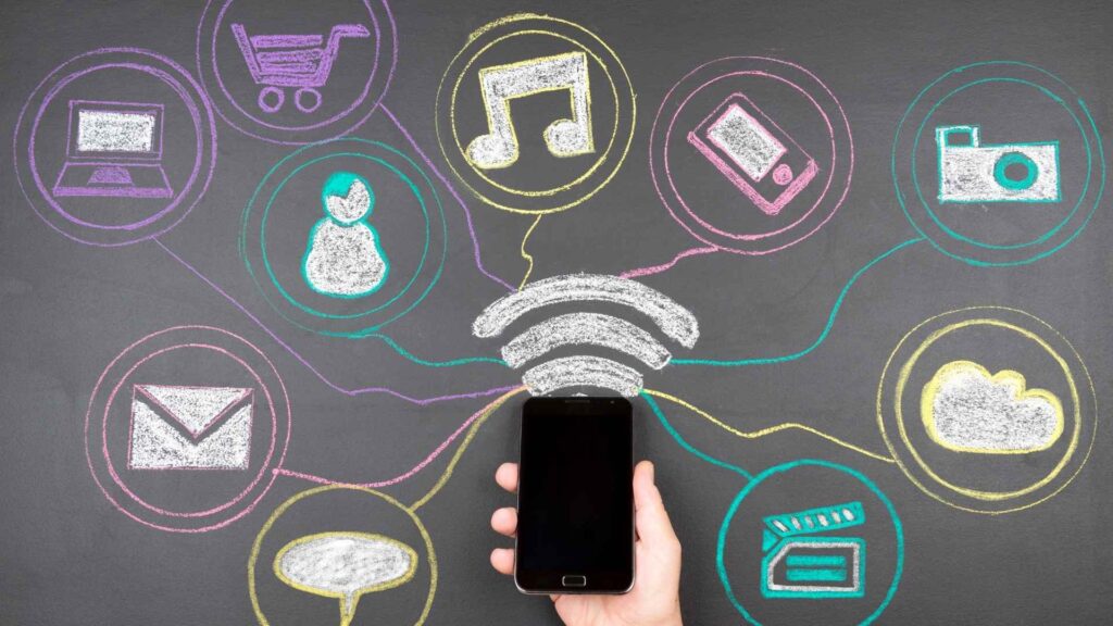 A hand holding a smartphone with colorful chalk drawings of icons such as shopping carts, music notes, and email around it