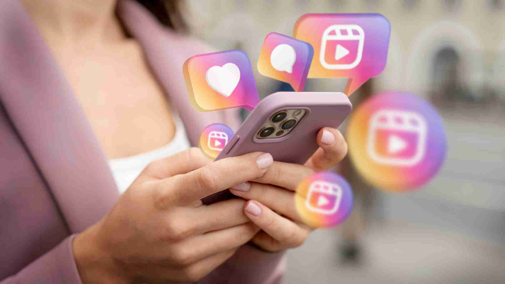 Close-up of a person wearing a mauve blazer holding a smartphone, with floating Instagram-style icons showing hearts, comments, and Reels videos