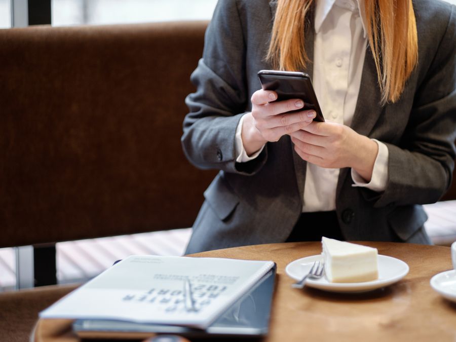 Businesswoman using smartphone in a café, with slice of cake and coffee.