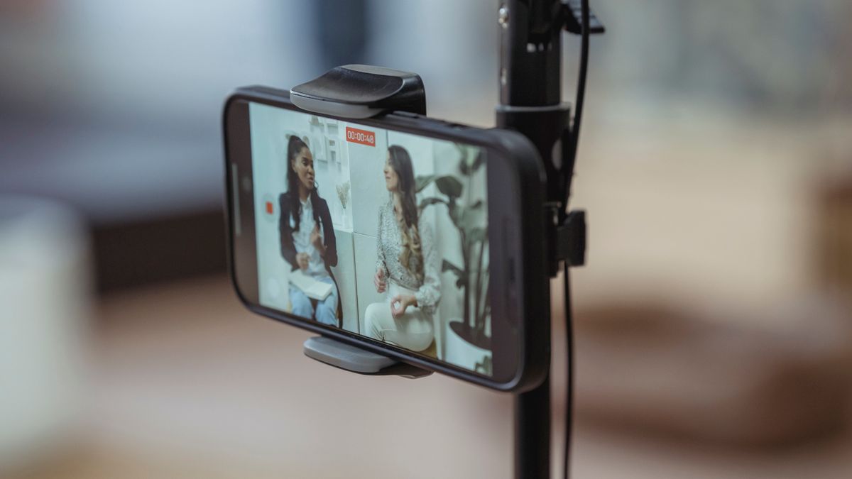 Modern smartphone on tripod recording video of content stylish women having friendly conversation