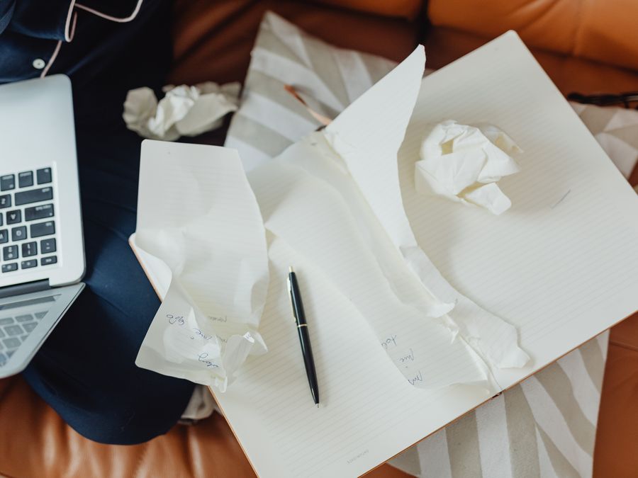 A creative workspace featuring a laptop, crumpled papers, and an open notebook with a pen, showcasing brainstorming or writing activities.