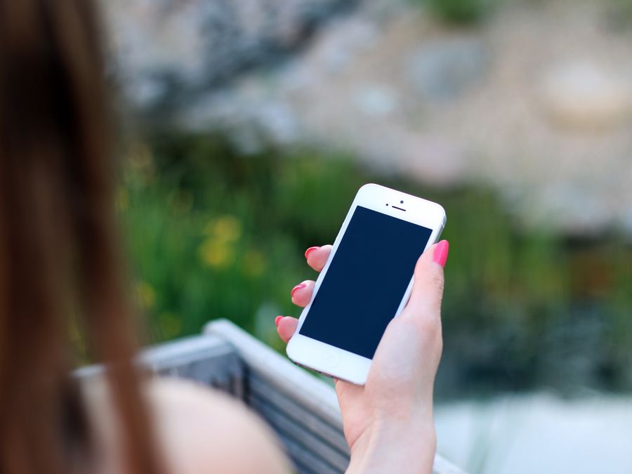 Woman using smartphone with blank screen, perfect for adding graphics. Outdoor lifestyle concept.