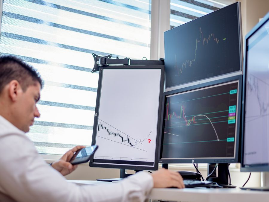 A stock trader analyzes financial data on multiple computer screens in an office setting.