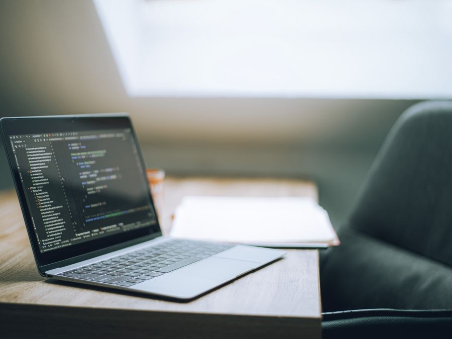 Open laptop displaying code on desk in bright, modern office setting. Ideal for tech and remote work context.