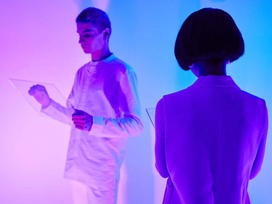 Two individuals interact with digital interfaces in a colorful futuristic setting.