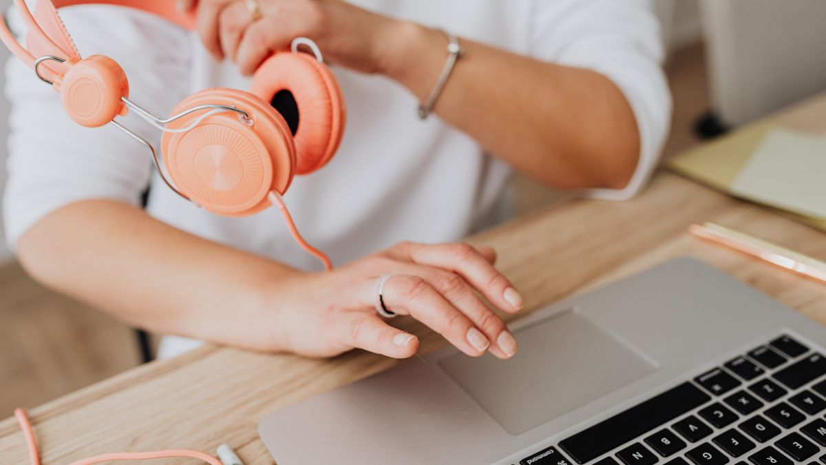Person holding headphones while using laptop, close-up view.