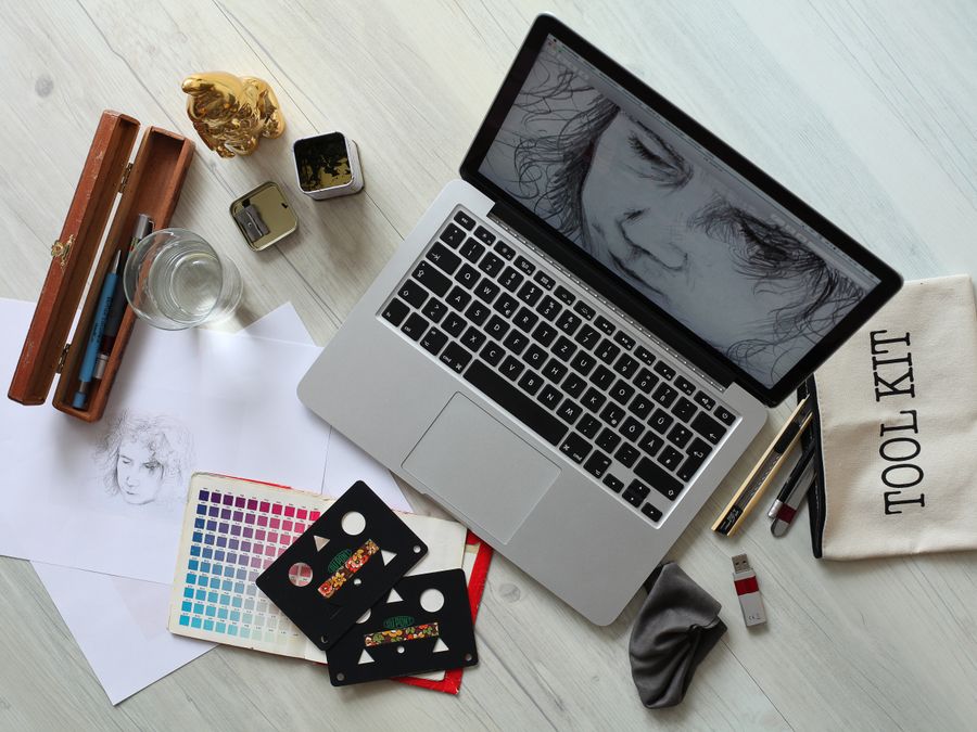 Top view of a creative workspace with a laptop, sketch supplies, and color palette.