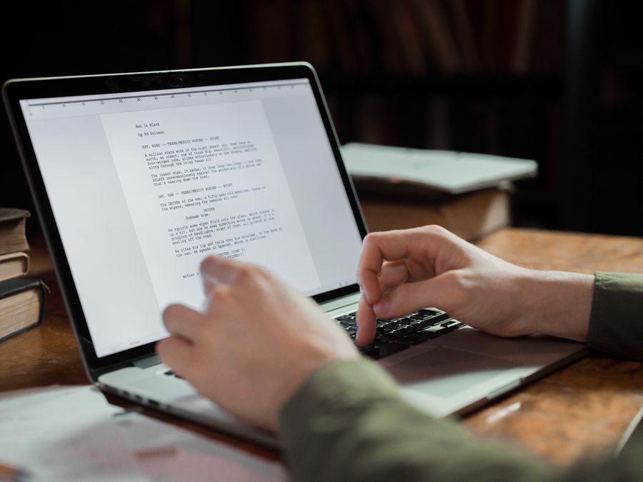 A person typing on a laptop in a cozy workspace with books around. Perfect for writing and technology themes.