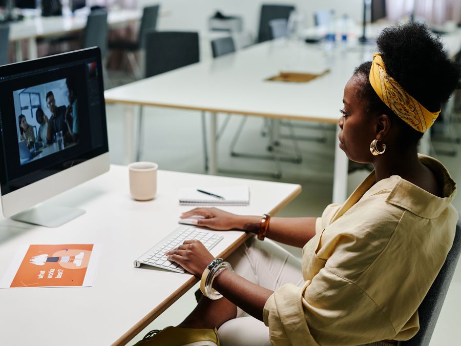Young black woman using computer for video editing in a modern office setting.