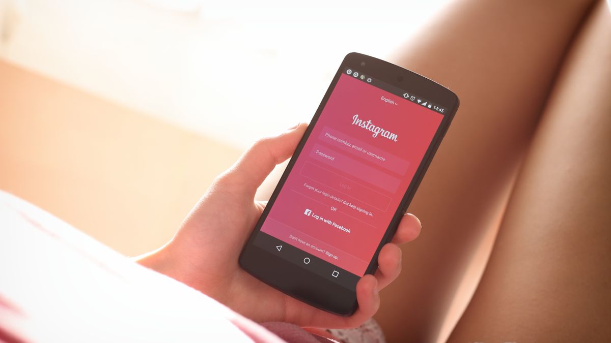 Woman holding a smartphone with Instagram login screen while relaxing indoors.