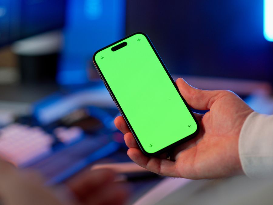 Hand holding a smartphone with a green screen in a modern indoor setting, ready for app design or mockup.