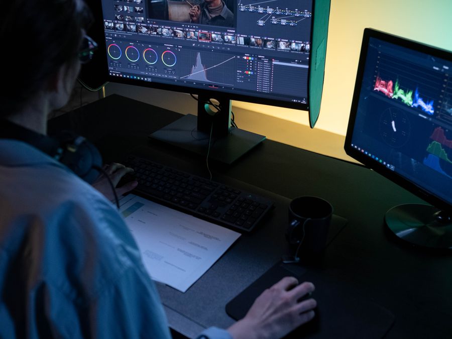 A video editor using dual monitors for editing footage in a dimly lit studio.