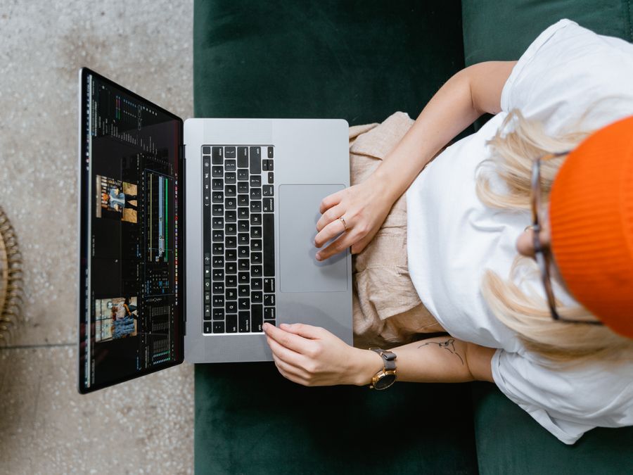 Top view of a woman editing video content on a laptop, wearing a casual outfit and orange beanie.