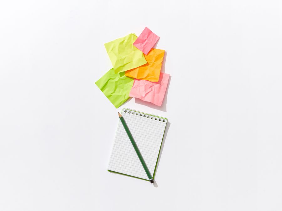 Colorful flat lay of crumpled sticky notes with a notepad and pencil on white background.