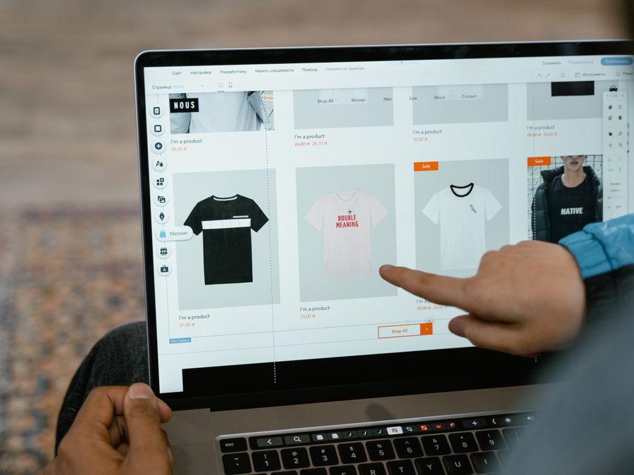A person points to t-shirt options in an online store on a laptop screen.