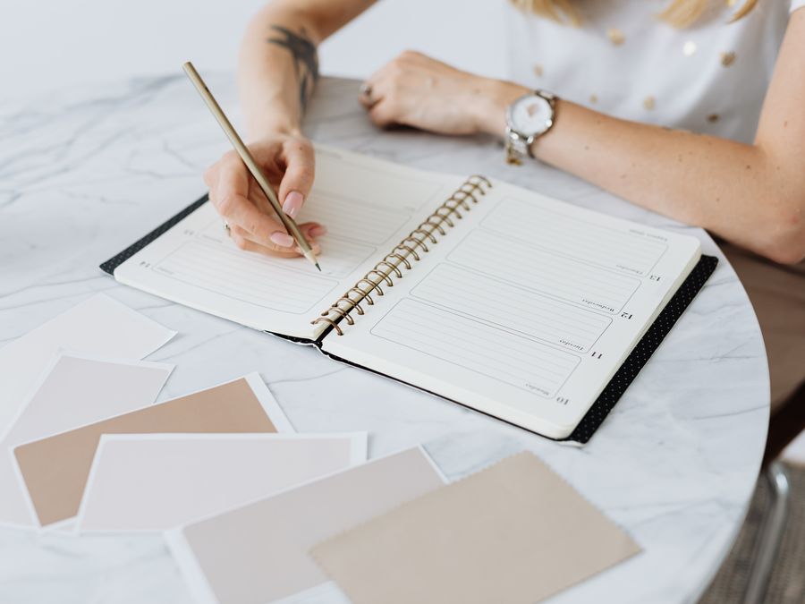 A woman writes in a planner on a marble table, surrounded by swatches. Creative and organized workspace.
