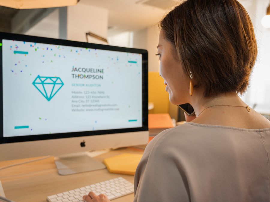 Businesswoman using a desktop computer in an office, viewing contact details on screen.