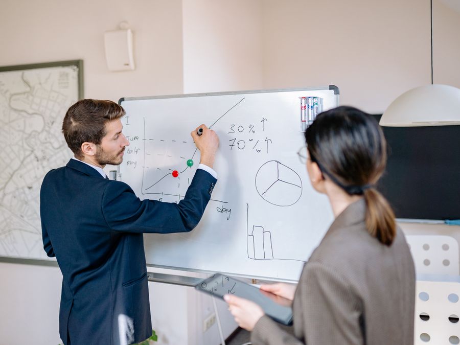 Two business professionals planning and discussing strategy at a whiteboard in a modern office setting.