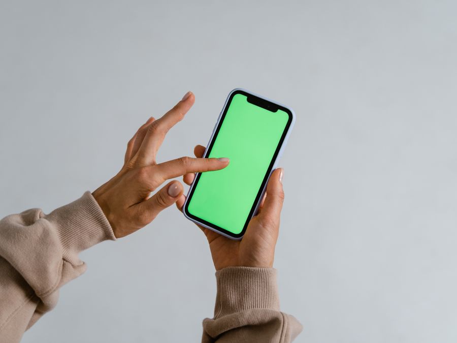 Hands interacting with a smartphone showcasing a vibrant green screen for multimedia use.