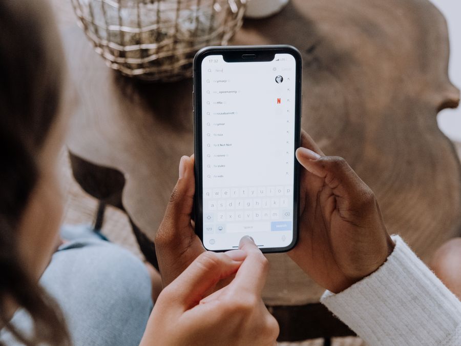 Close-up of hands holding a smartphone, searching for apps like TikTok on a wooden table.