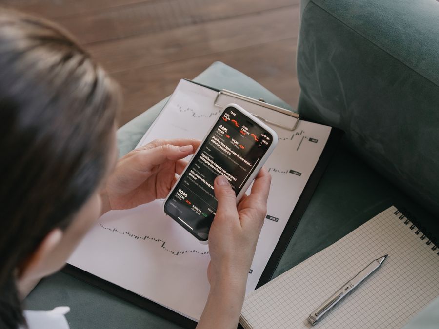 A woman reviews financial data on her smartphone with charts and graphs around her for stock market analysis.