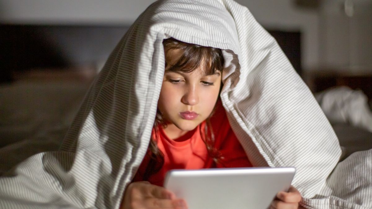 Child using a tablet under a blanket in bed, focused and engaged at night.