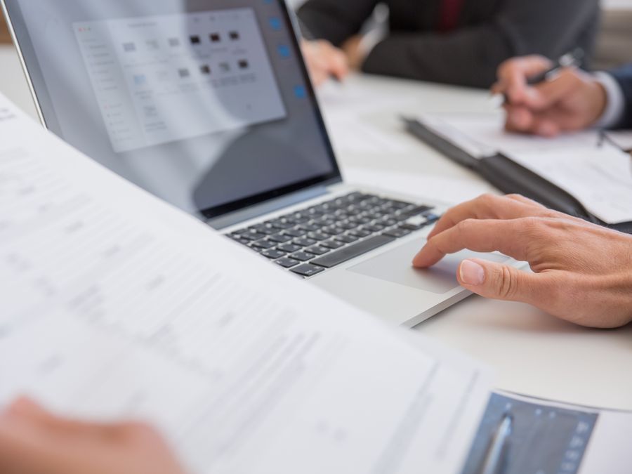 Close-up of hands working on documents and a laptop in an office setting, illustrating teamwork and productivity.