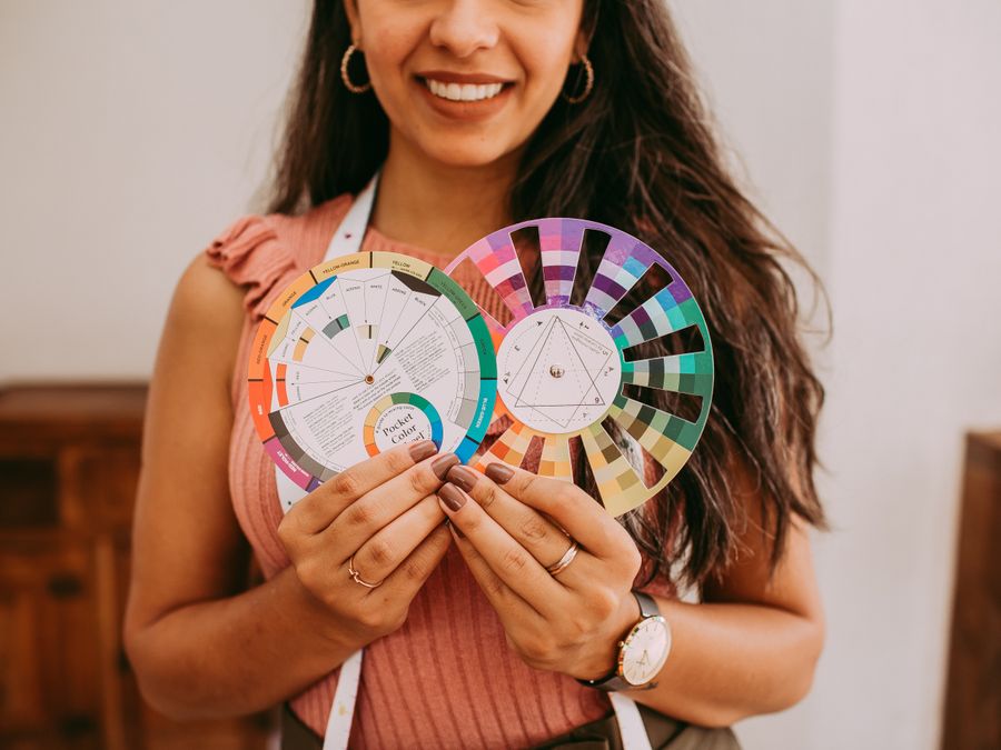 Smiling woman holding vibrant color wheel palettes indoors, showcasing creative design inspiration.
