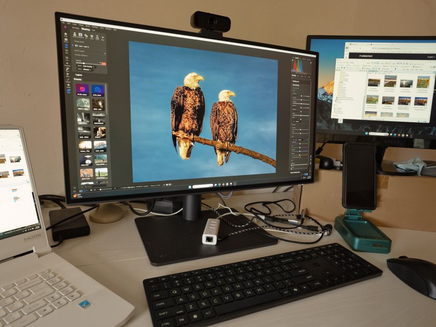A desk setup showing photo editing software on multiple monitors, a keyboard, and peripherals.