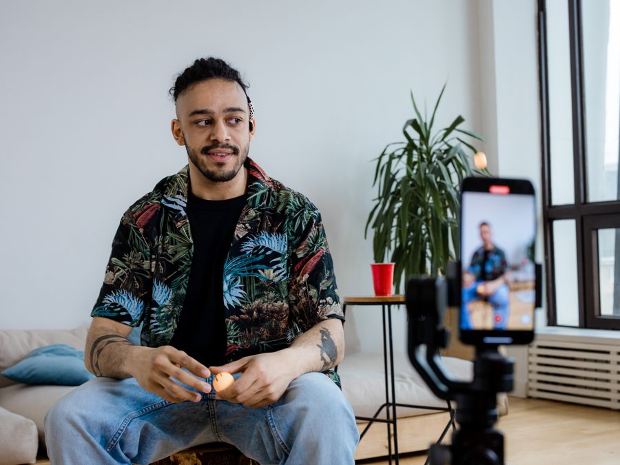 A young man recording video content indoors with a smartphone and tripod.