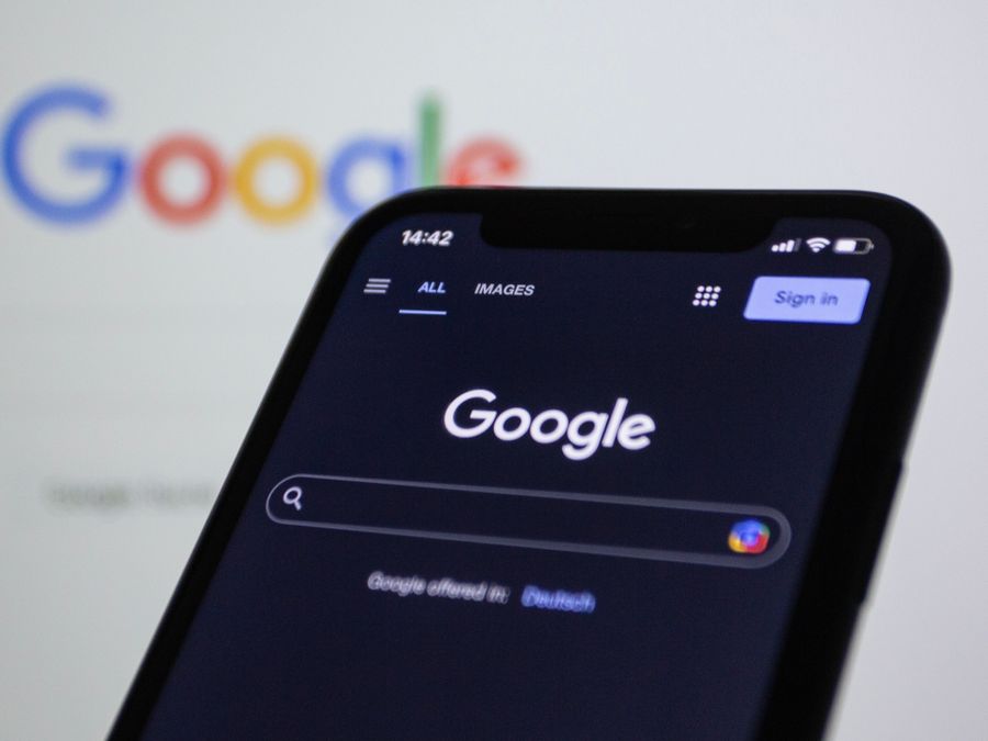 Smartphone screen showing Google search in dark mode with the Google logo in the background.