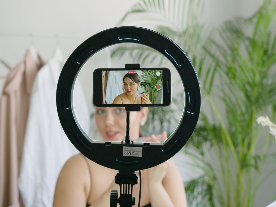 Woman creating video content using smartphone and ring light setup indoors.