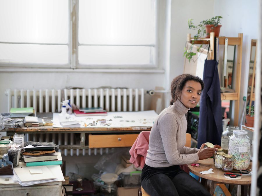 A woman in a creative workspace surrounded by art supplies and plants, exuding creativity and focus.
