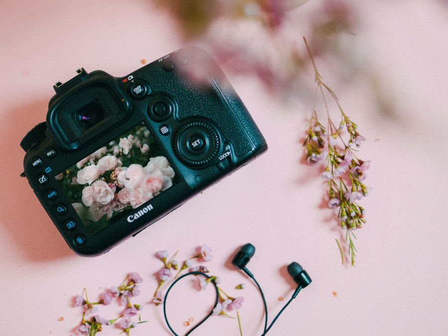 Flat lay of camera with floral theme on pink with headphones.