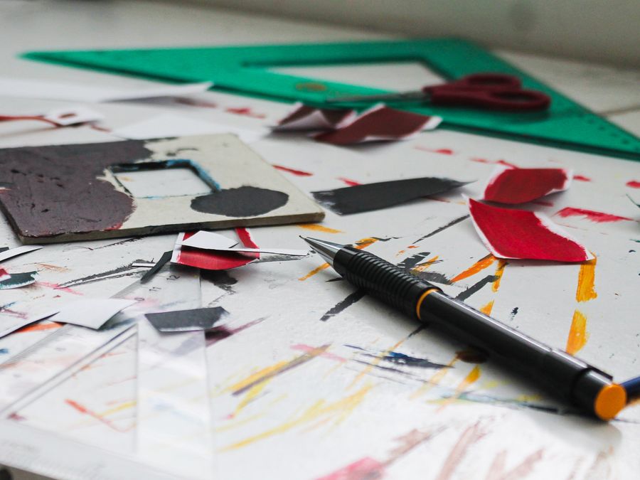 A colorful art workspace with cut paper, a pen, and drafting tools.