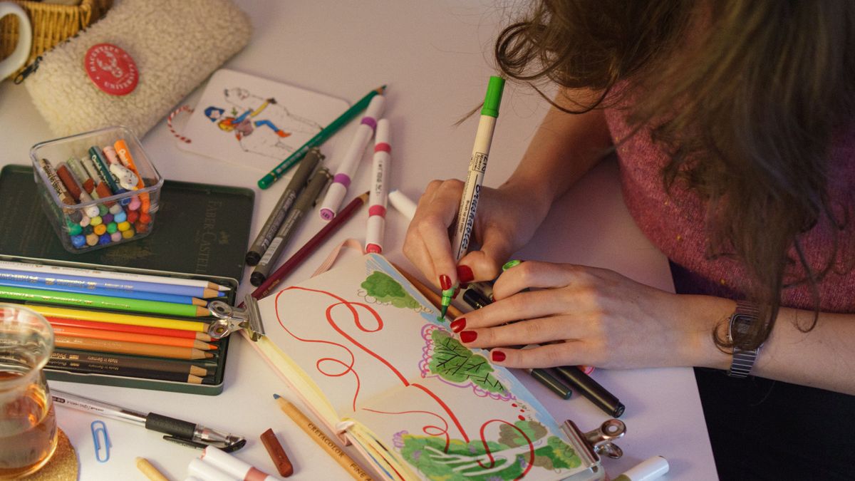 Colorful artistic workspace depicting a person drawing with markers and pencils.