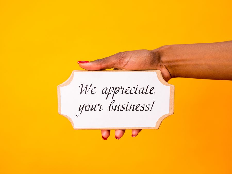 A hand holding a thank you sign with 'We appreciate your business!' on a vibrant yellow background.