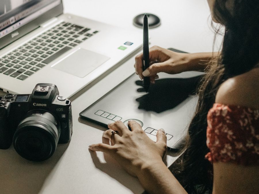 Close-up of a woman using a graphics tablet to create digital art with a laptop.