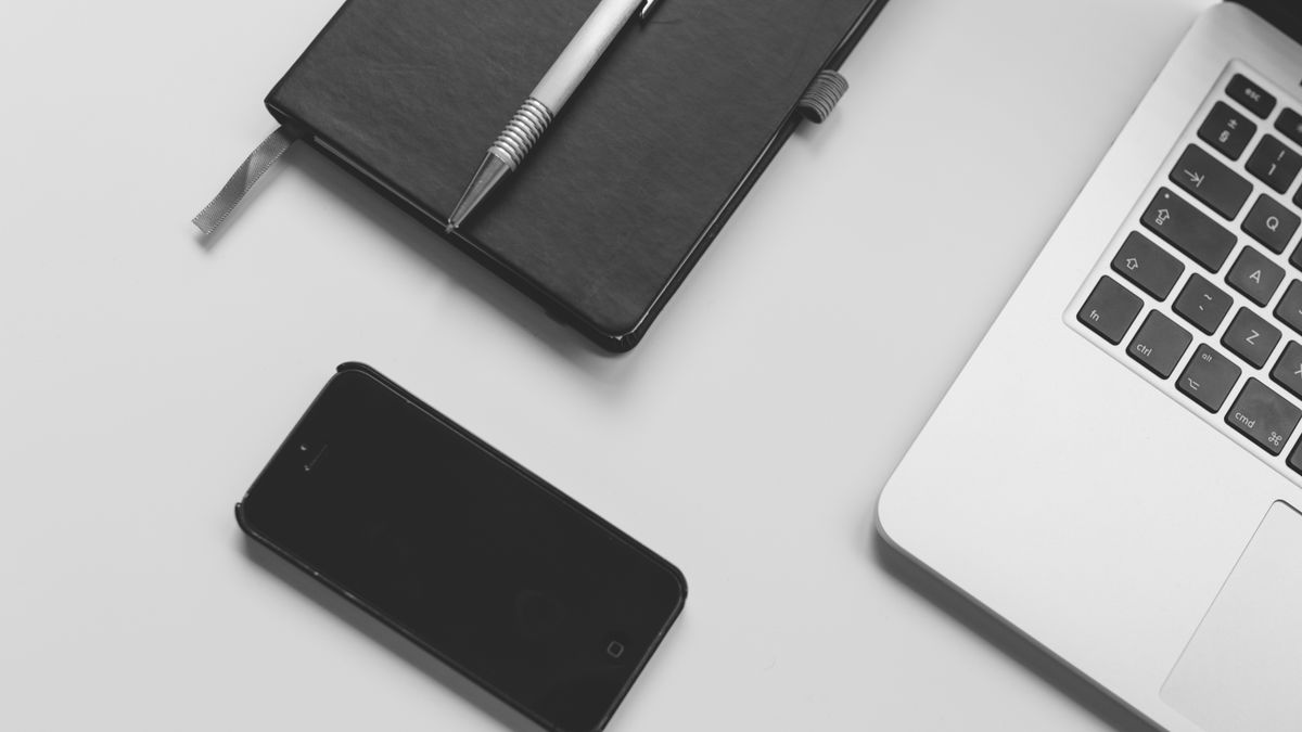 Black notebook with pen, smartphone, and laptop on a clean white desk. Perfect for business and tech themes.