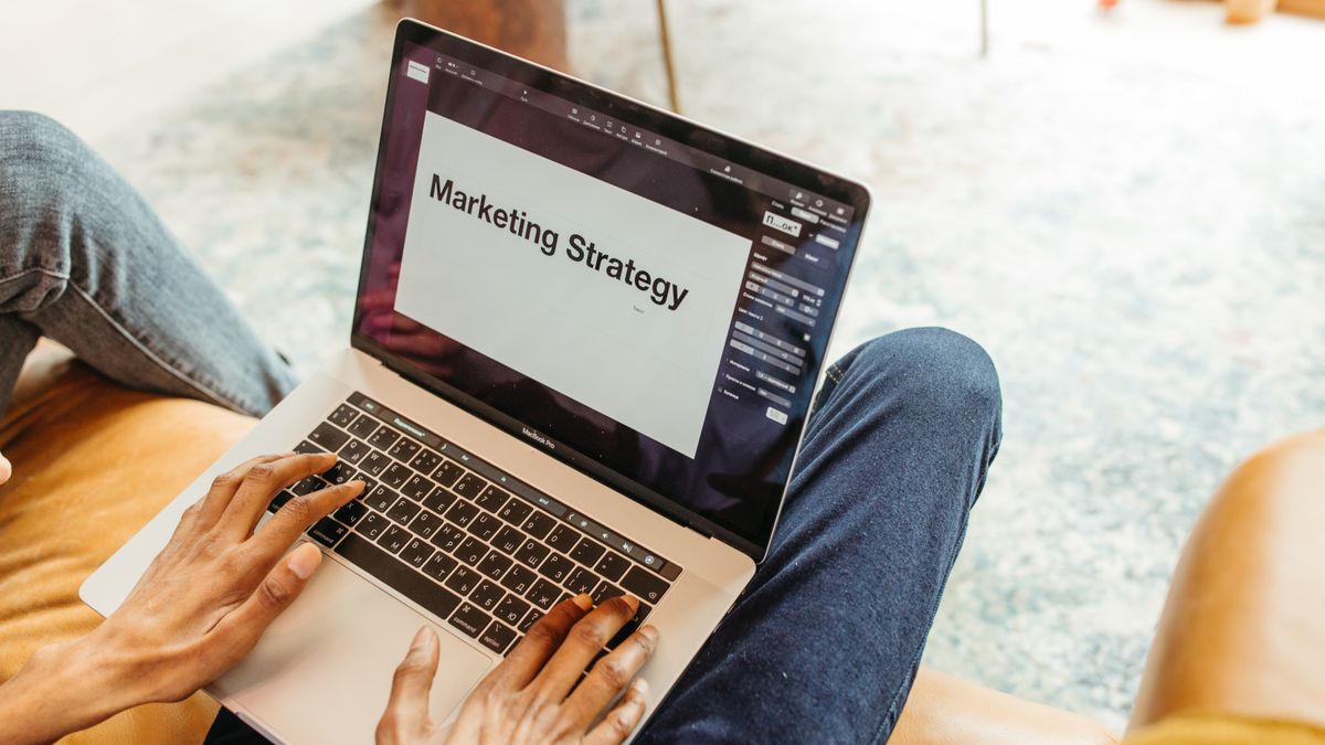 Close-up of hands using a laptop displaying a marketing strategy presentation indoors.