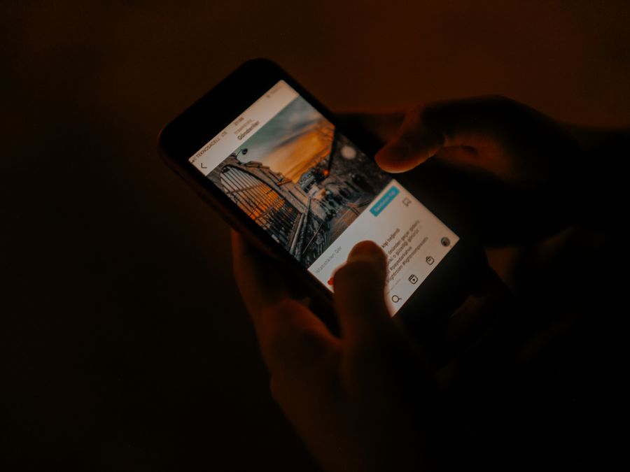 Hands holding a smartphone browsing social media in low light.