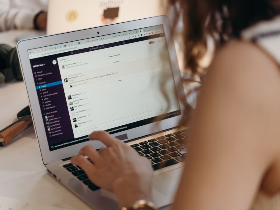 A businesswoman typing on a laptop in an office setting, using Slack for communication.