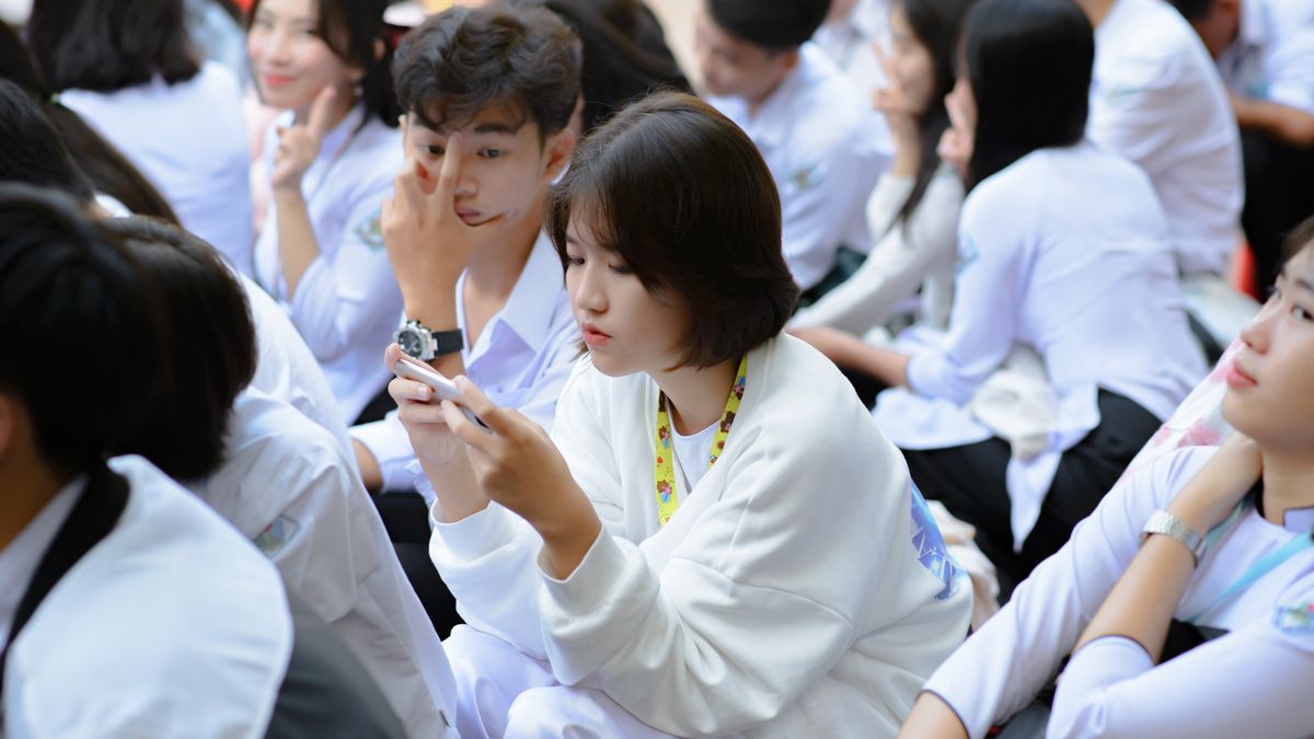 Group of students sitting outdoors, using smartphones and engaging with technology.