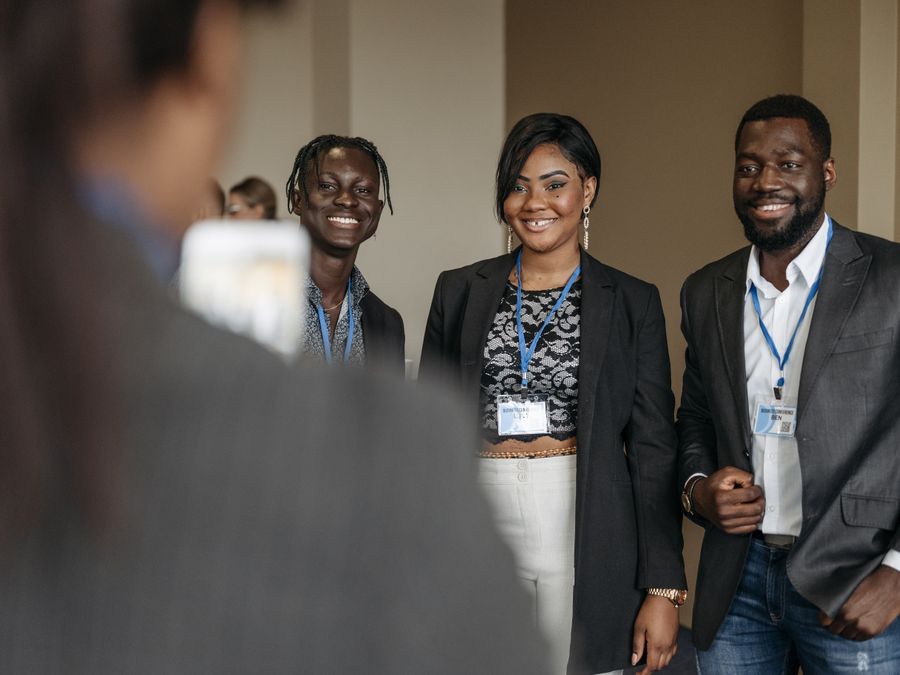 Three business professionals smiling at a corporate event, wearing formal attire and badges.
