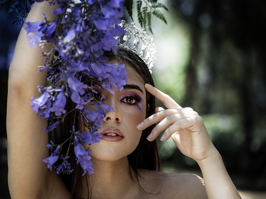 Elegant portrait of a woman with purple flowers and crown outdoors.