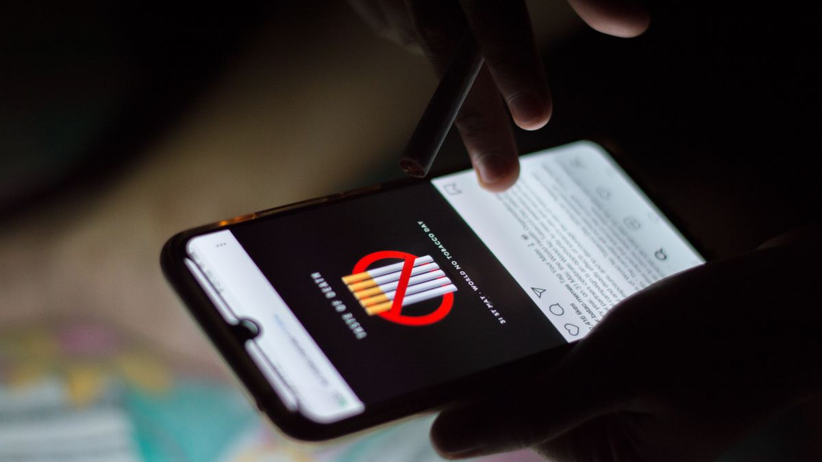 A person browsing social media on a smartphone at night, holding a cigarette.