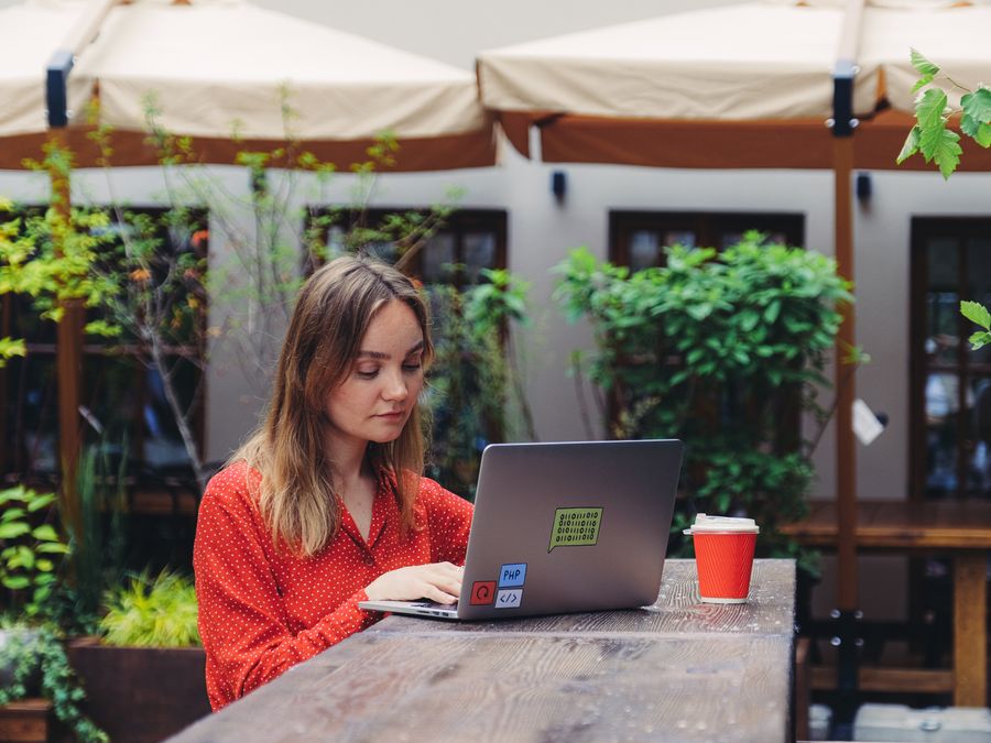 Young woman working on a laptop in an outdoor cafe setting, enjoying a cup of coffee.