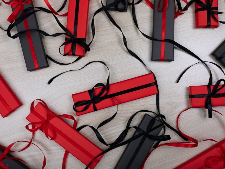An artistic flat lay of red and black gift boxes with ribbons on a wooden tabletop.