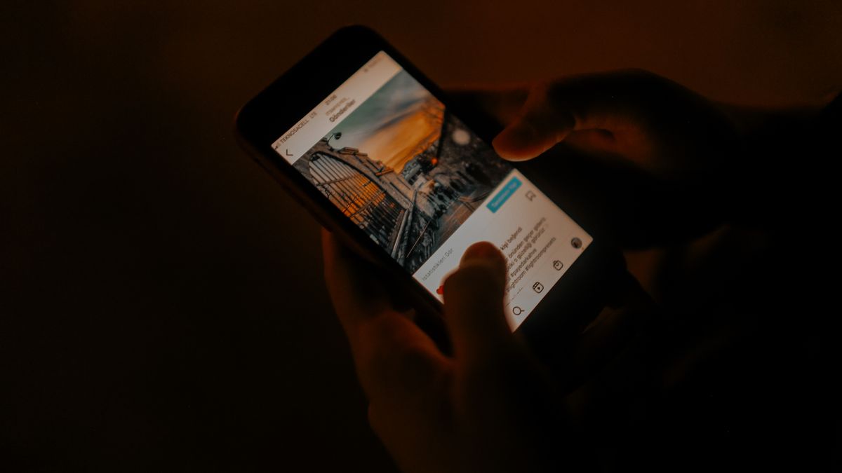 Hands holding a smartphone browsing social media in low light.